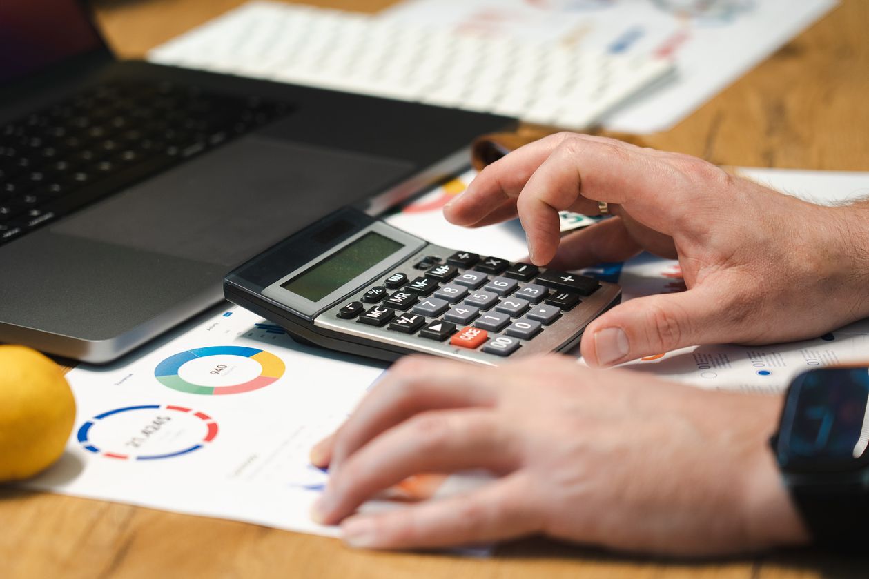 Close-up of hands using a calculator alongside spreadsheets and a pen